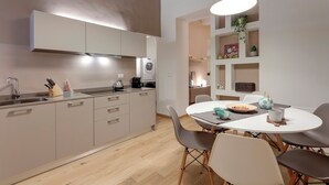 Een moderne keuken met een ingebouwde wasmachine, een eethoek met een ronde tafel en stoelen, en een plank met decoratieve objecten.