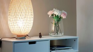 Een lamp met een geweven patroon, een vaas met bloemen en een stapel boeken op een witte plank.