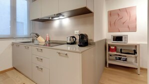 Een moderne keuken met een ingebouwde kookplaat, magnetron en koffiezetapparaat. Er ligt een houten vloer en een raam zorgt voor natuurlijk licht.