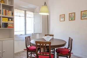 A dining area with a round table, four wooden chairs with red cushions, a hanging lamp, and a bookshelf with books. - Mamo Florence - Borgo Santa Croce Apartment (Florence)