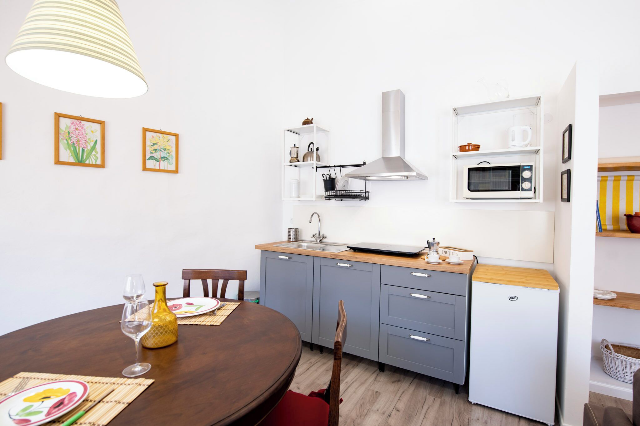 A compact kitchen with a microwave, stove, and sink. There is a dining table with chairs and a vase.