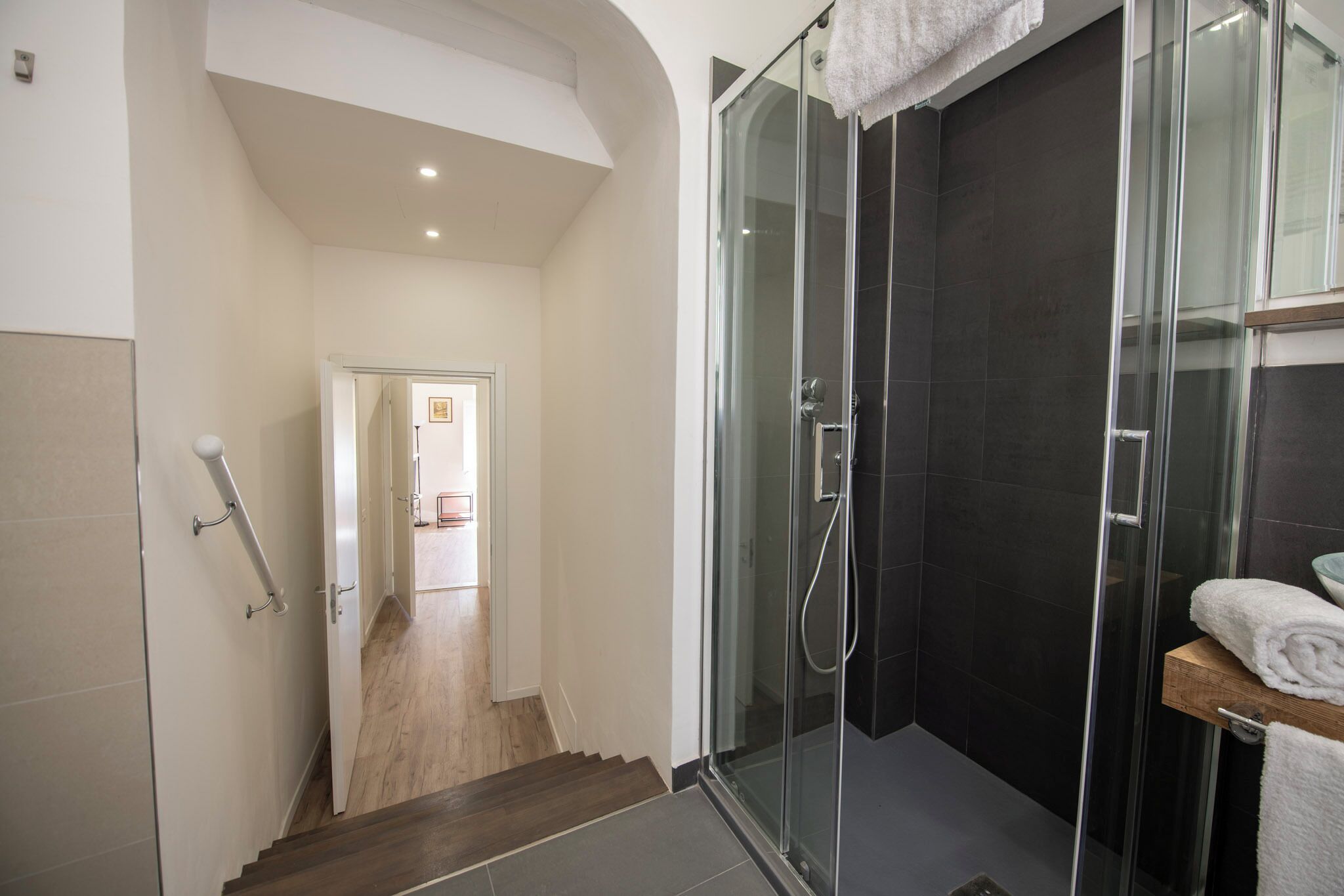 Ein modernes Badezimmer mit Duschkabine aus Glas, einer Holztreppe und einem sichtbaren Waschtisch mit einem Handtuch.