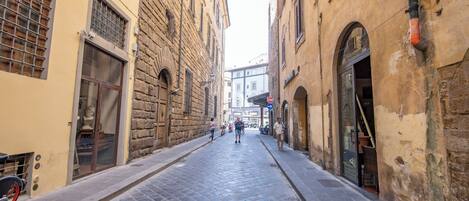 A narrow cobblestone street flanked by historic buildings with arched doorways and large windows.