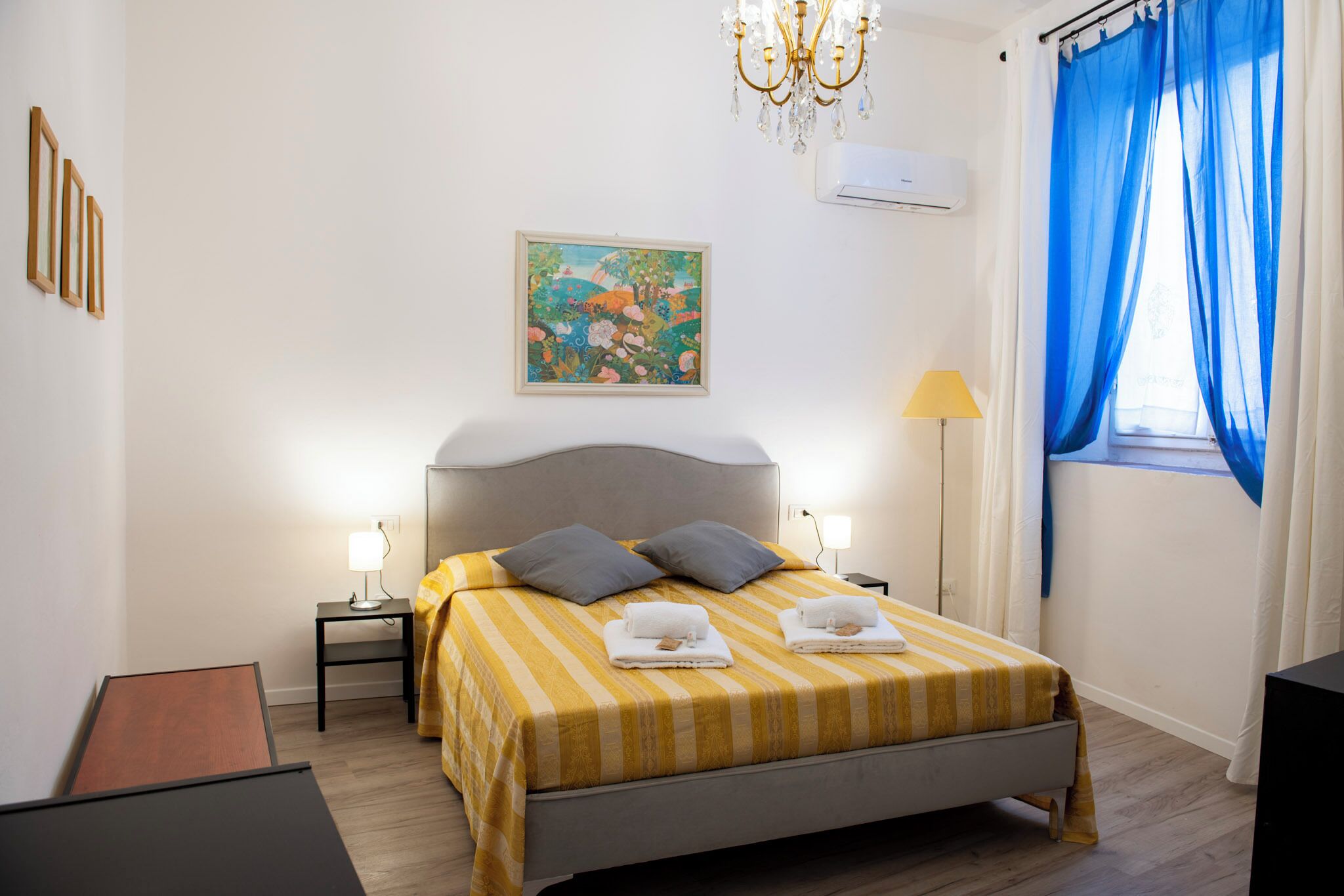 Une chambre d’hôtel avec un lit, deux lampes de chevet, un tableau au mur et une fenêtre avec des rideaux bleus.