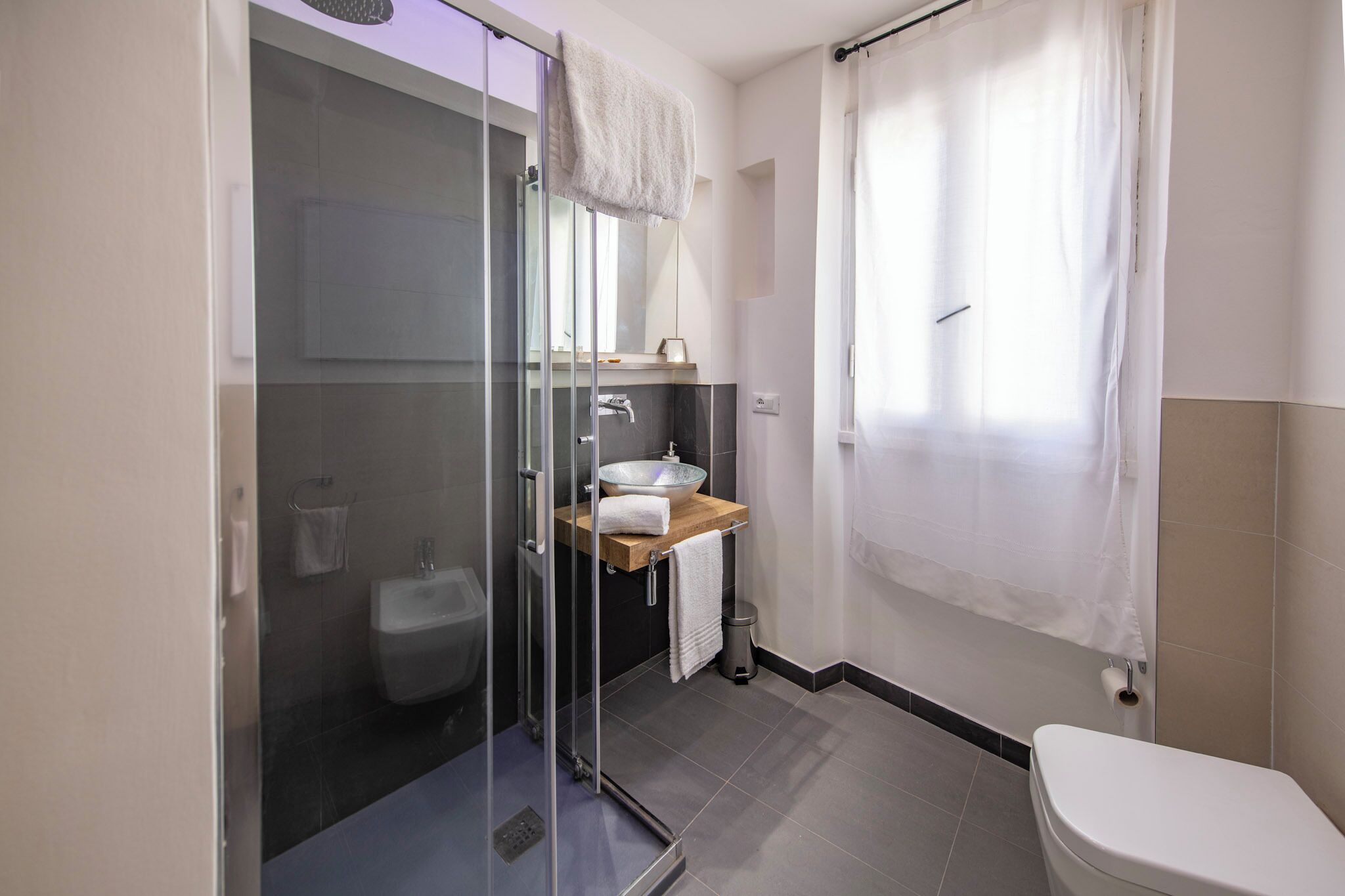 A modern bathroom with a glass-enclosed shower, a wooden vanity, and a white toilet.