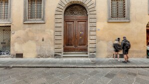 A building with a large wooden double door, a stone archway, and two windows with metal bars. - Mamo Florence - Casper Apartment (Florence)
