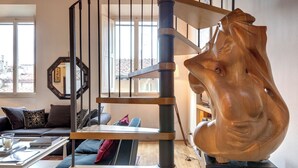 A modern living room with a wooden staircase, a large wooden sculpture, and a sofa with cushions. - Mamo Florence - Casper Apartment (Florence)
