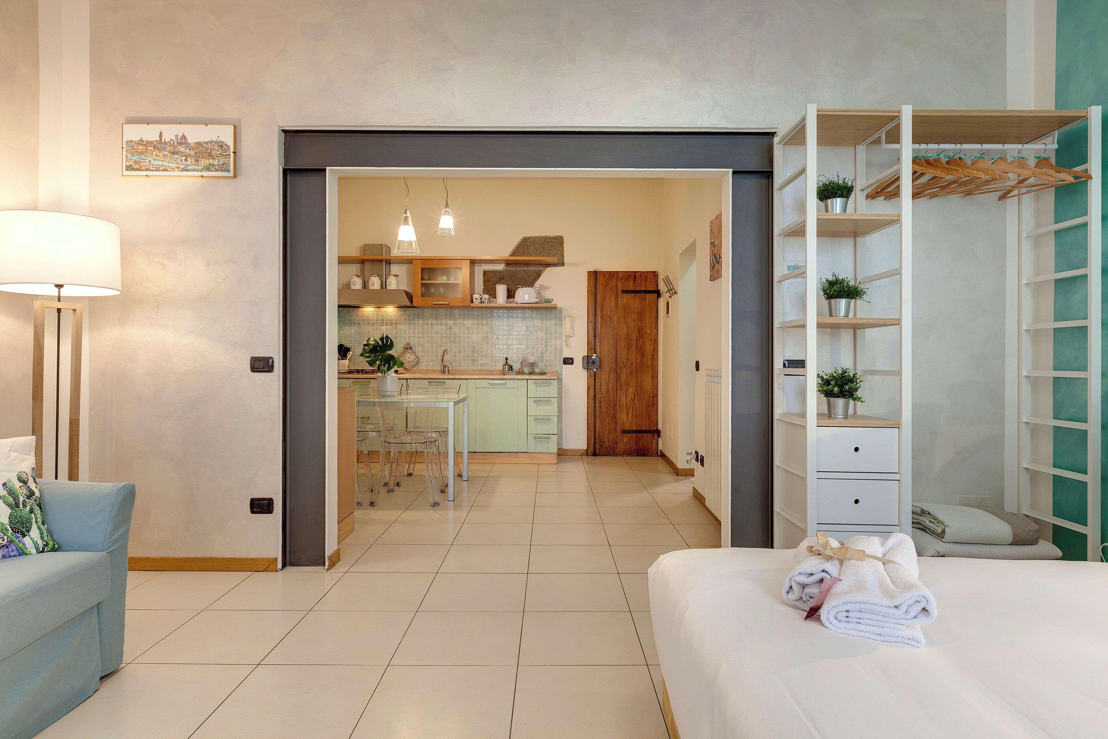 A modern hotel room with a bed, a desk, and a kitchenette.