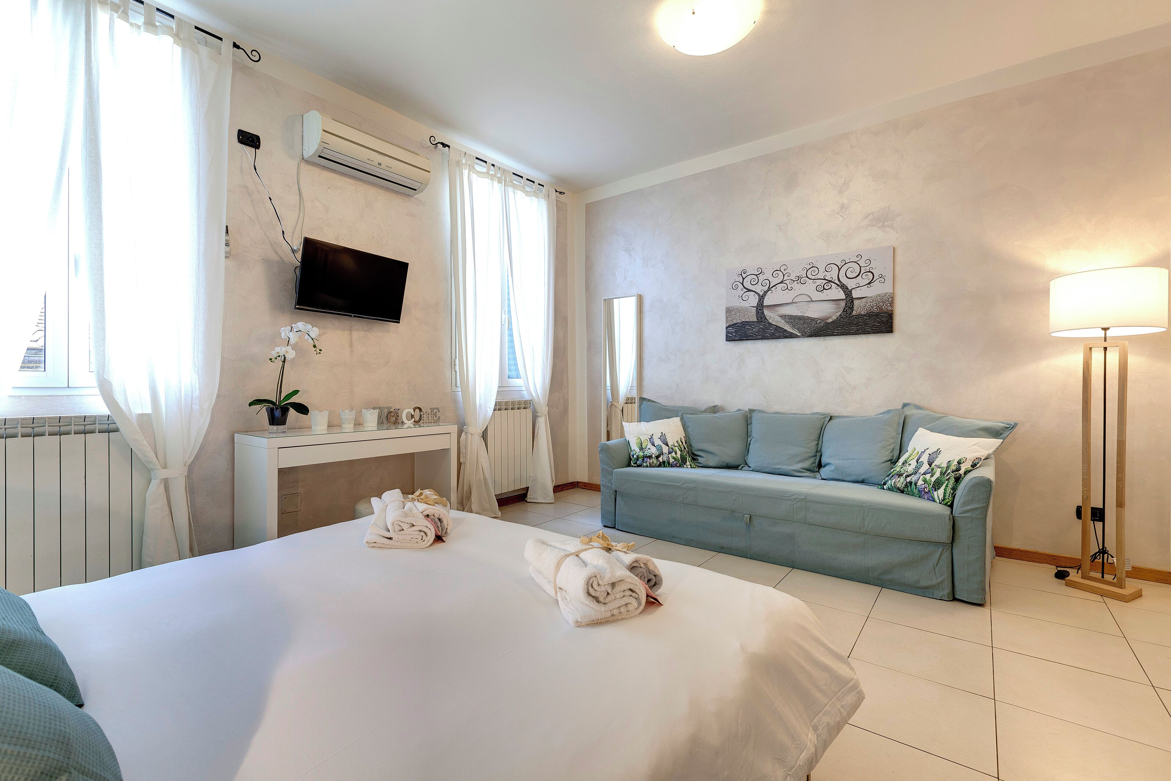 A hotel room with a bed, a sofa, a TV, a painting, and a lamp.