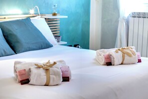 A neatly made bed with white linens and two rolled towels with 'Excellent' branding, a bedside table with a glass, and a blue pillow. - Mamo Florence - Charlize Apartment (Florence)