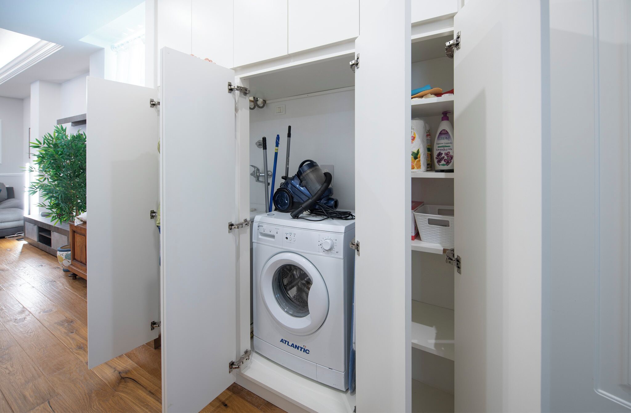A compact laundry room with a front-loading washing machine, a vacuum cleaner, and storage shelves.