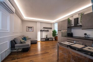 Una sala de estar moderna con un sofá gris, suelo de madera y una zona de comedor con mesa y sillas de vidrio.