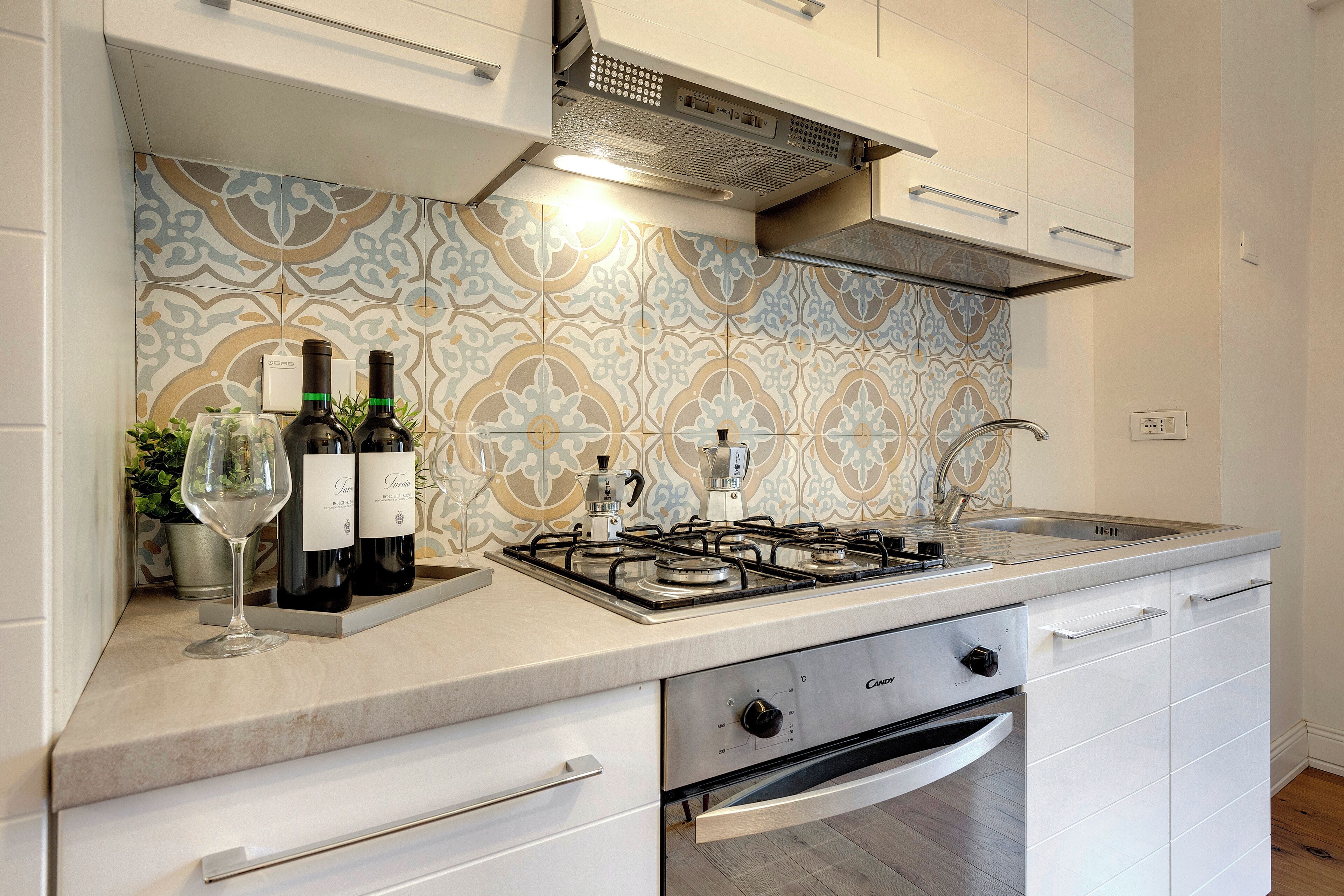 A modern kitchen with a gas stove, white cabinets, and patterned backsplash.