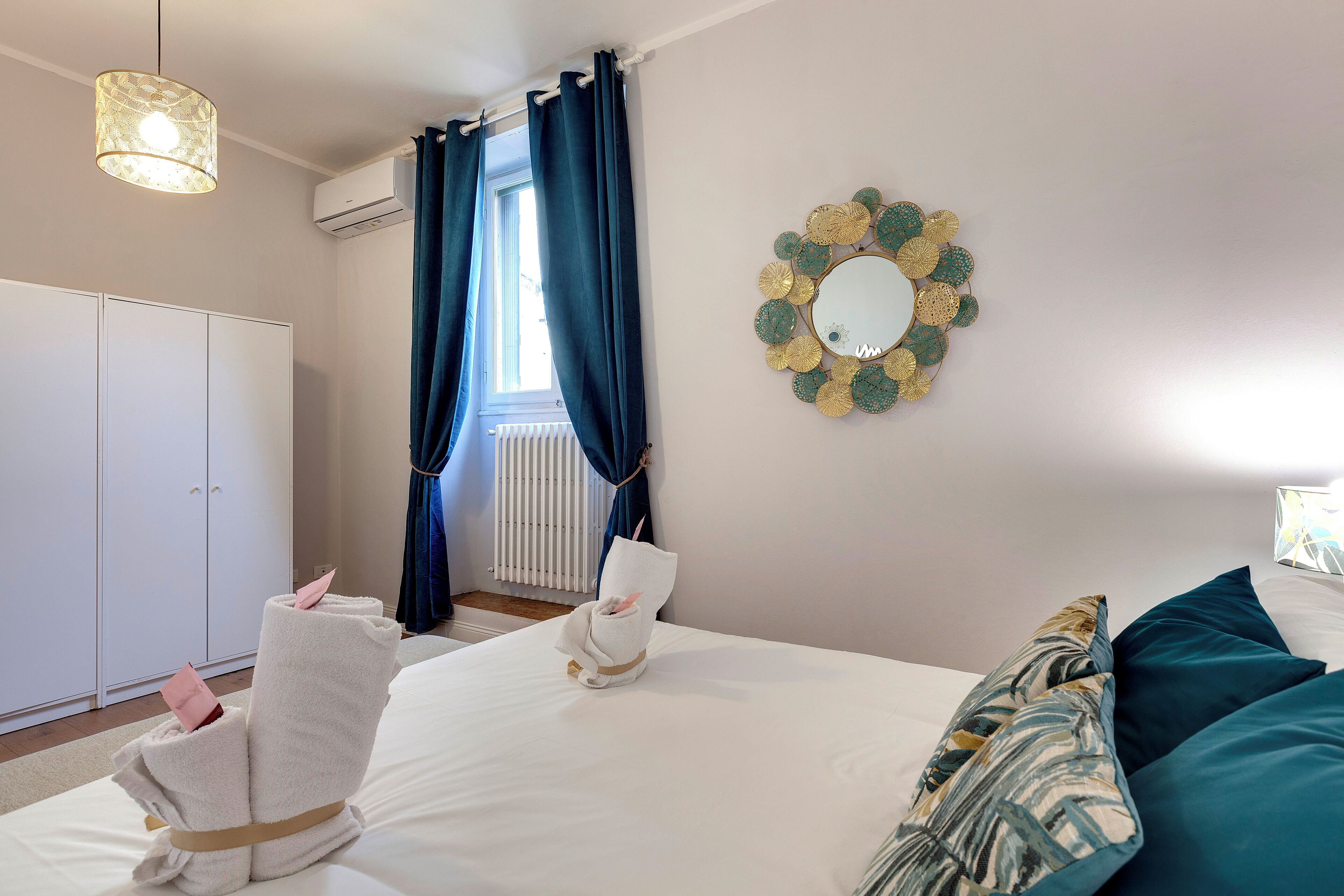 A hotel room with a bed, a wardrobe, a mirror, and a window with curtains.