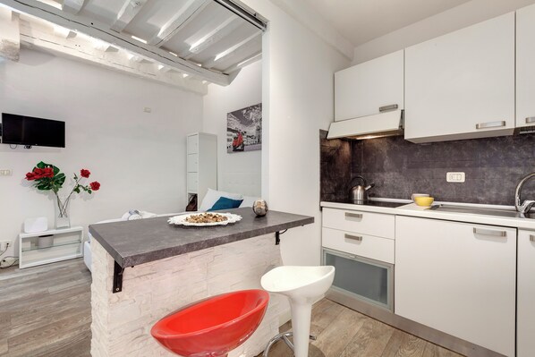A modern kitchen with white cabinets, a black countertop, and a red chair. - Mamo Florence - Cristofano Studio (Florence)