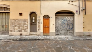 A building with a stone facade, a wooden door, and a garage door with graffiti. - Mamo Florence - Cristofano Studio (Florence)