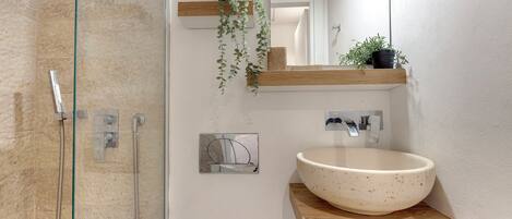 Een badkamer met een douchecabine van glas, een groot wastafelbak, houten planken met planten en een spiegel.
