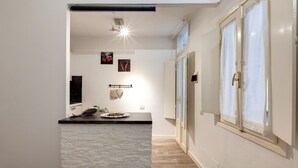 A modern kitchen with a stone island, a ceiling light, and a view of the adjacent room. - Mamo Florence - Cristofano Studio (Florence)