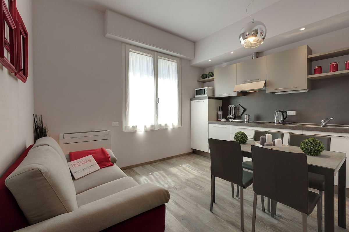 Un apartamento moderno con comedor, cocina y sala de estar con sofá y almohada roja.