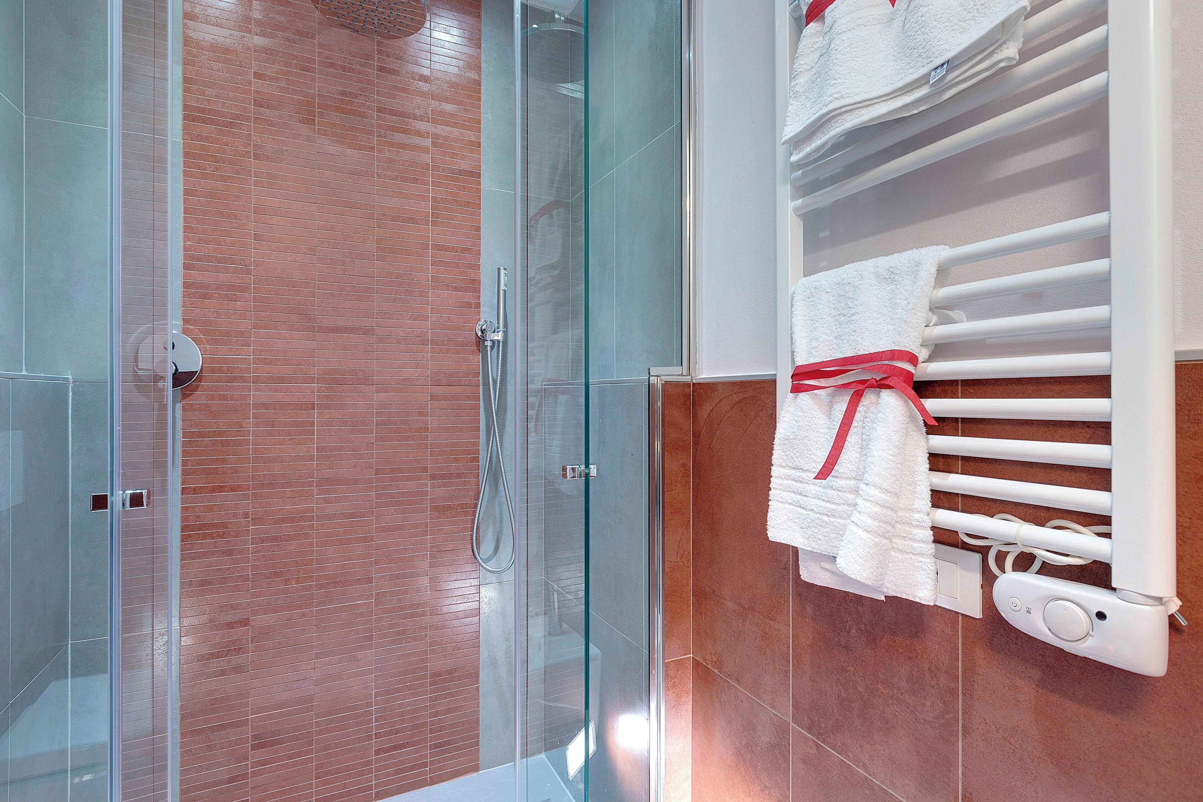Een moderne badkamer met een douche in glazen cabine, een handdoekrek met netjes gevouwen handdoeken, en een witte radiator.
