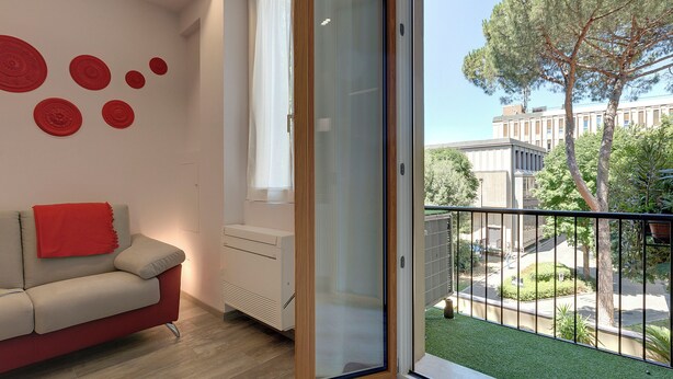 A modern living room with a red sofa, a glass door leading to a balcony, and decorative red circular wall art. - Mamo Florence - Dante & Virgilio Apartments (Florence)