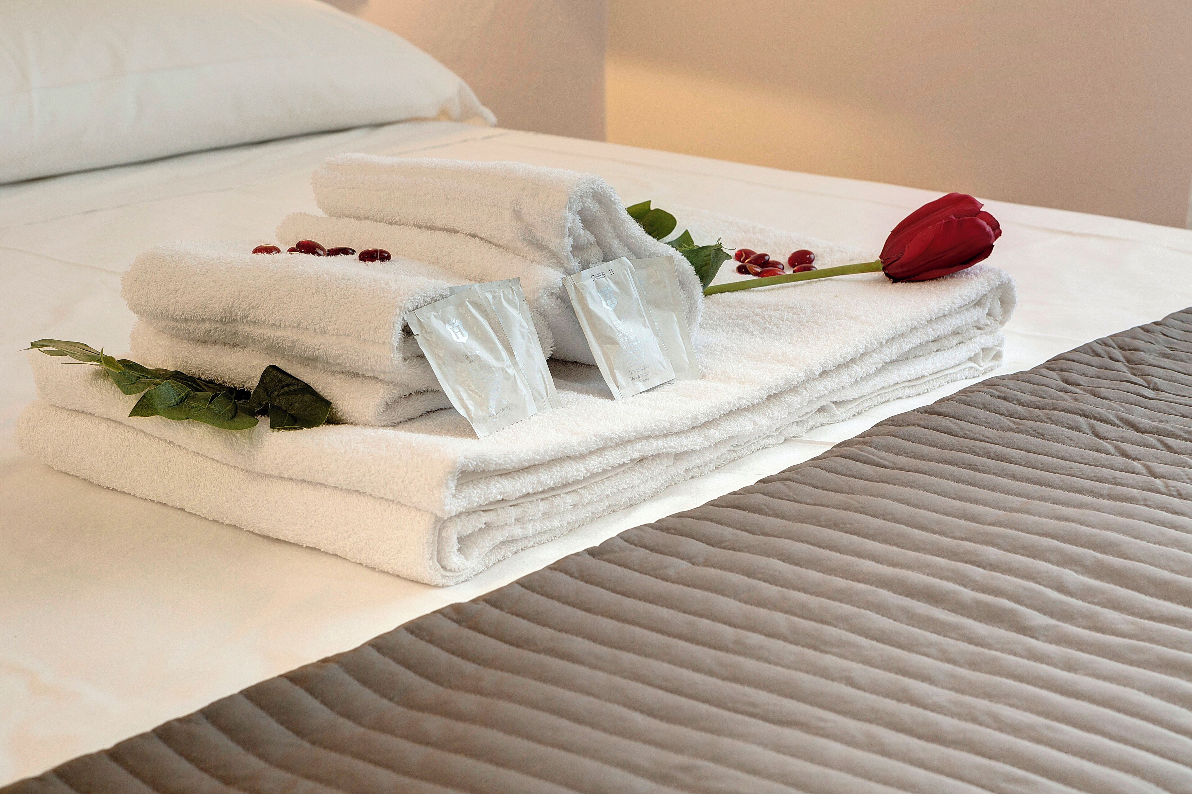A neatly folded set of white towels on a bed with a red rose and green leaves.