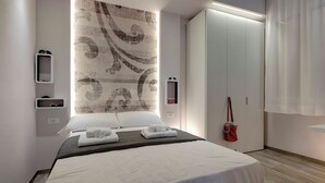 A modern hotel room with a large bed, a wardrobe, a mirror, and a wall with a decorative pattern. - Mamo Florence - Dante & Virgilio Apartments (Florence)