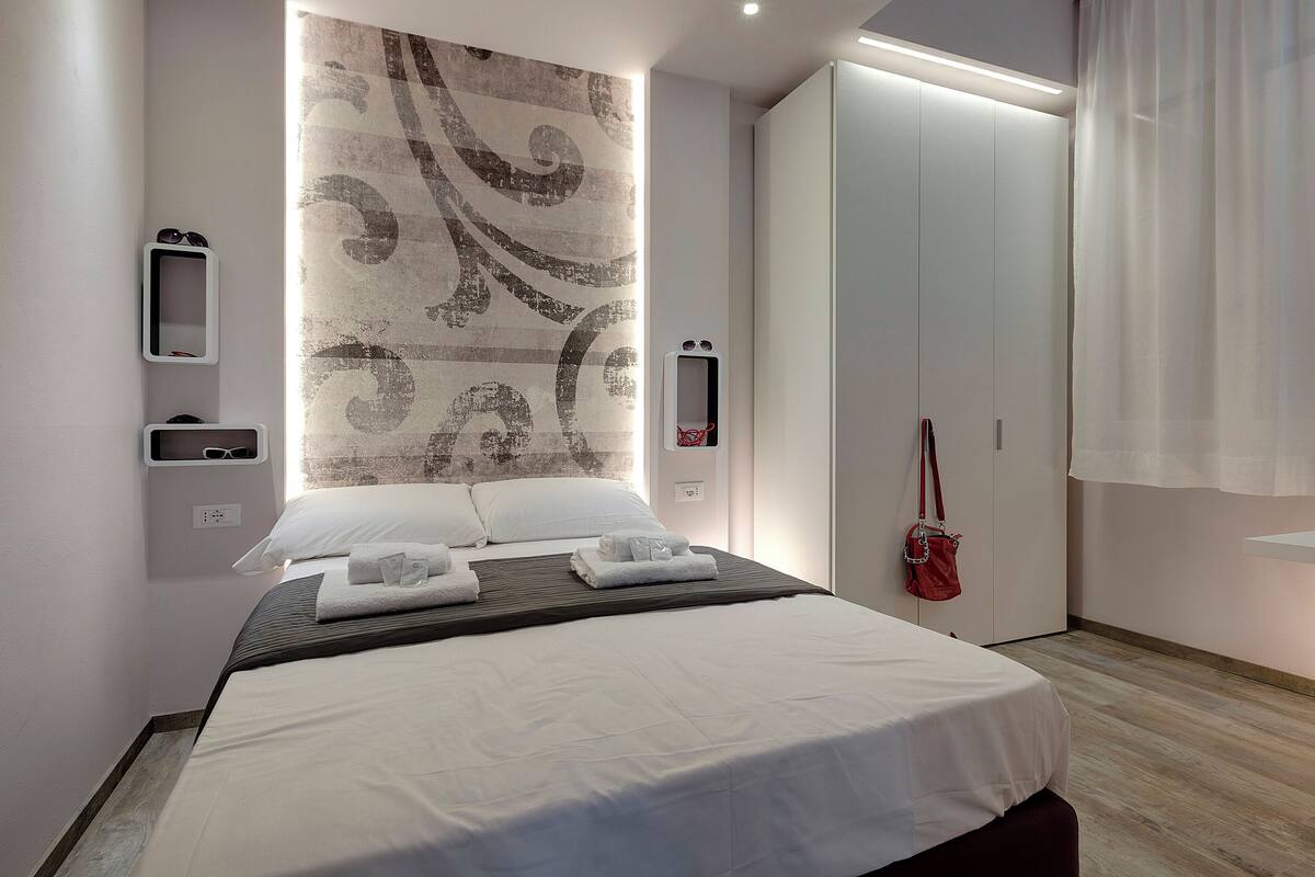 Una habitación de hotel moderna con una cama grande, un armario, un espejo y una pared con un diseño decorativo.