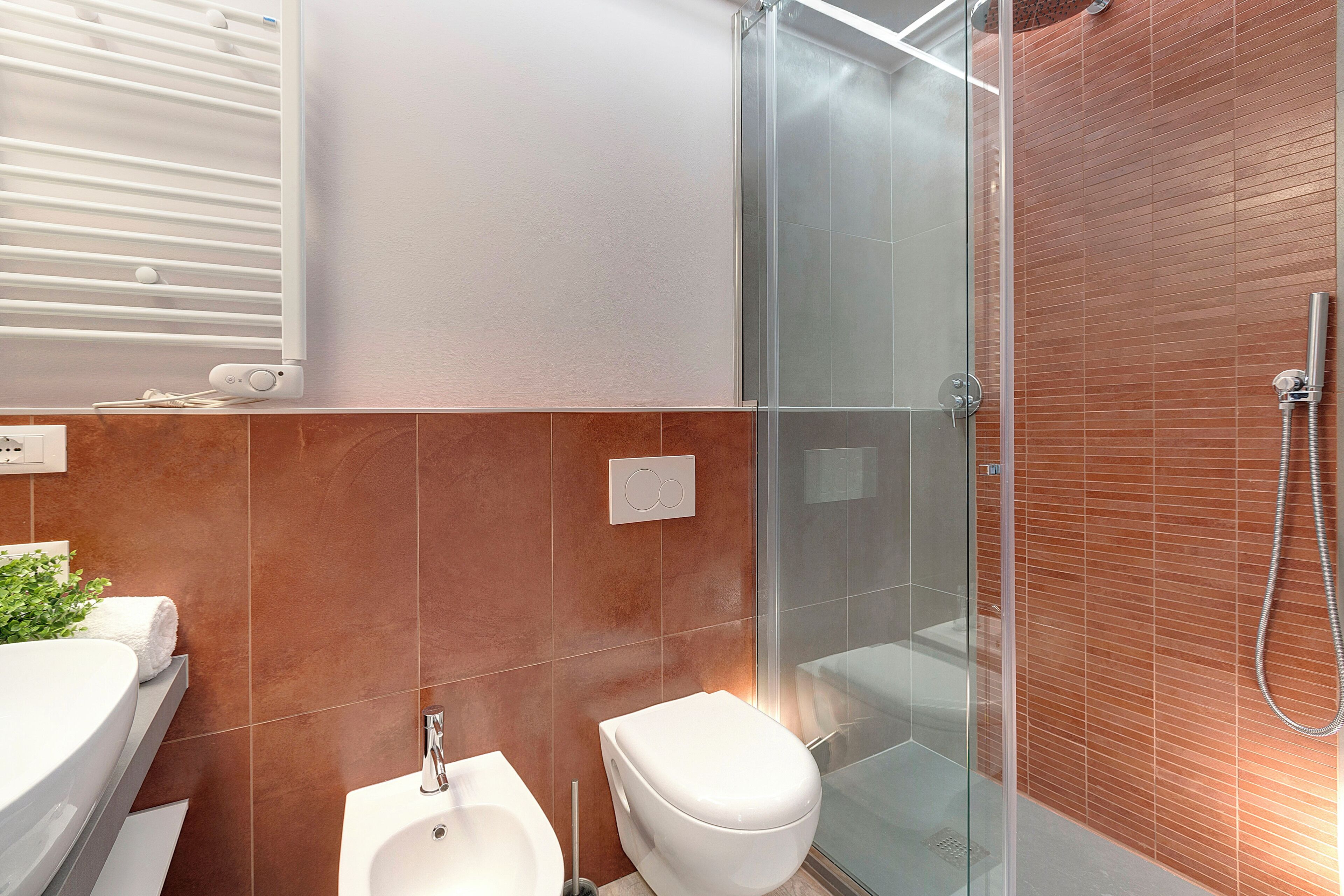 A modern bathroom with a glass shower enclosure, a white toilet, and a sink with a towel.