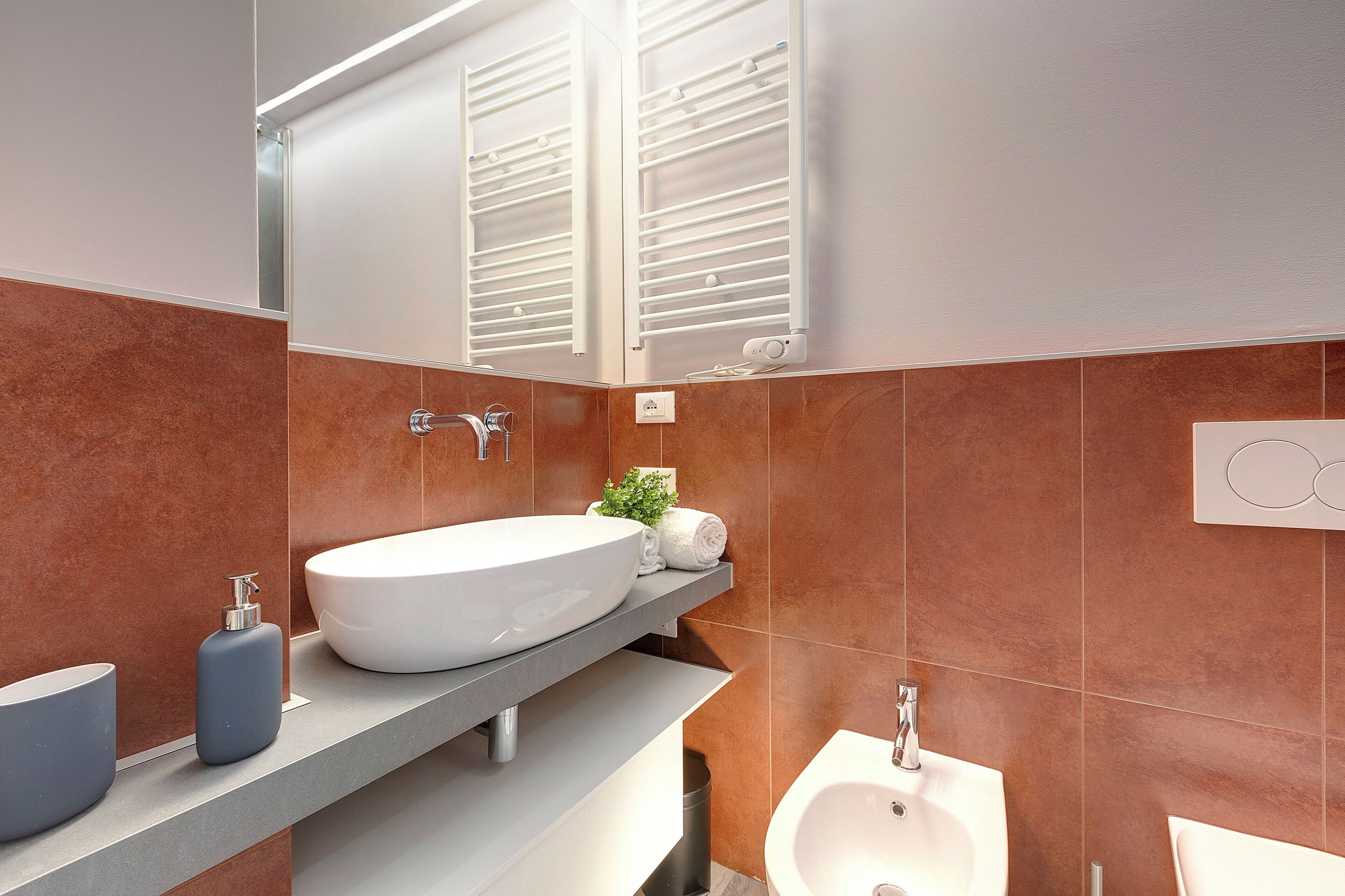 Un baño moderno con un lavamanos grande blanco, un lavamanos más pequeño, un bidé y un toallero.