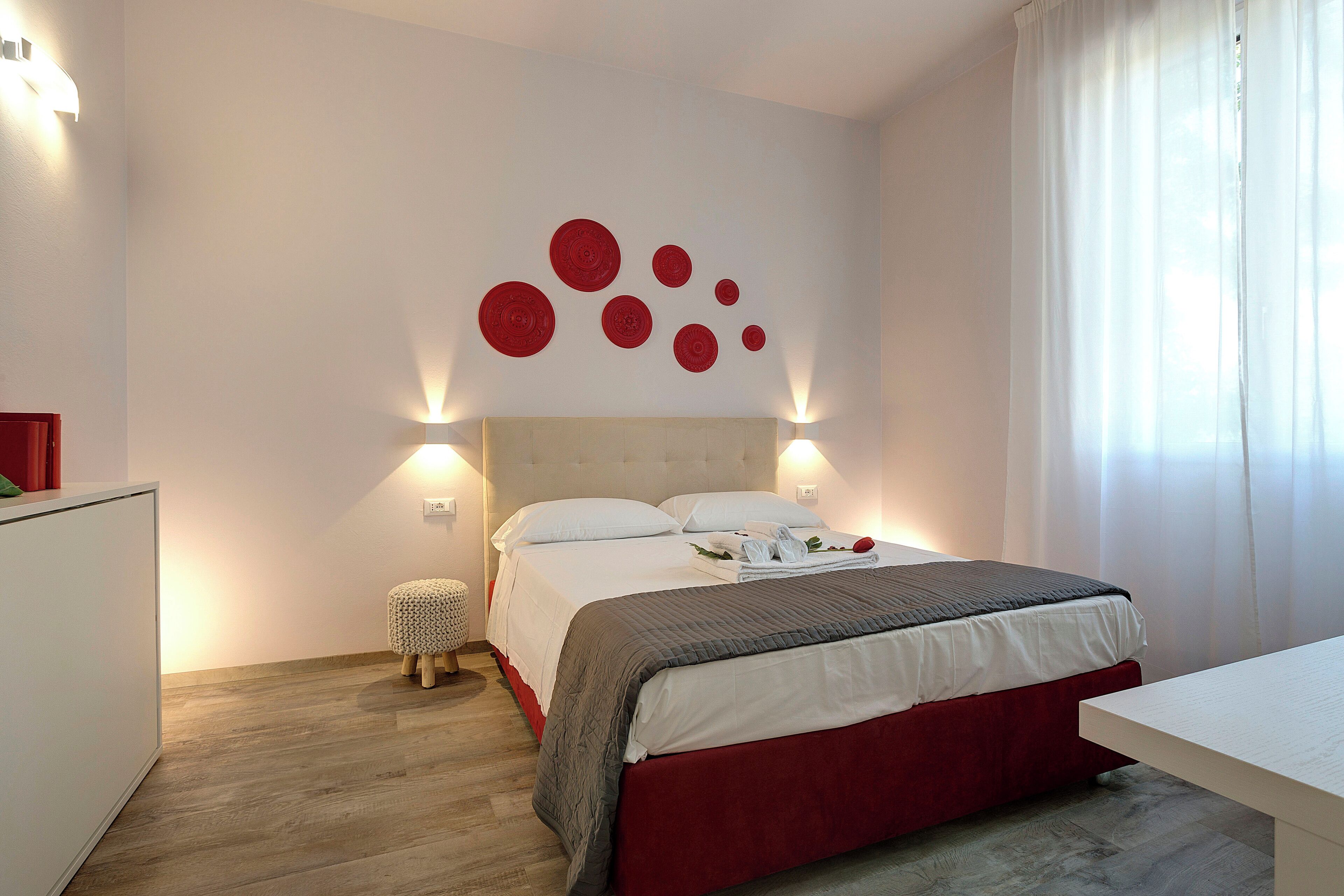 A hotel room with a bed, bedside table, and a small stool.