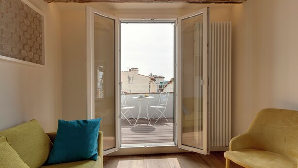 Una habitación con un sofá verde, un sillón amarillo y un ventanal corredero que da a un balcón con mesa y sillas.