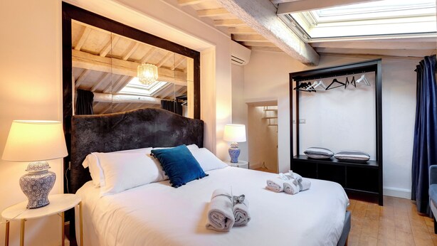 Habitación de hotel con una cama grande, dos lámparas de noche, un espejo, un armario y una percha para ropa.