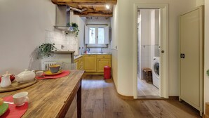 Kapea keittiö, jossa on puupalkit, pesuallas, pyykinpesukone ja ruokapöytä sekä teekuppisetti.