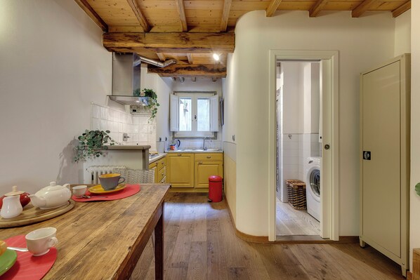 A narrow kitchen with wooden beams, a sink, a washing machine, and a dining table with tea set. - Mamo Florence - Diciotto Apartment (Florence)