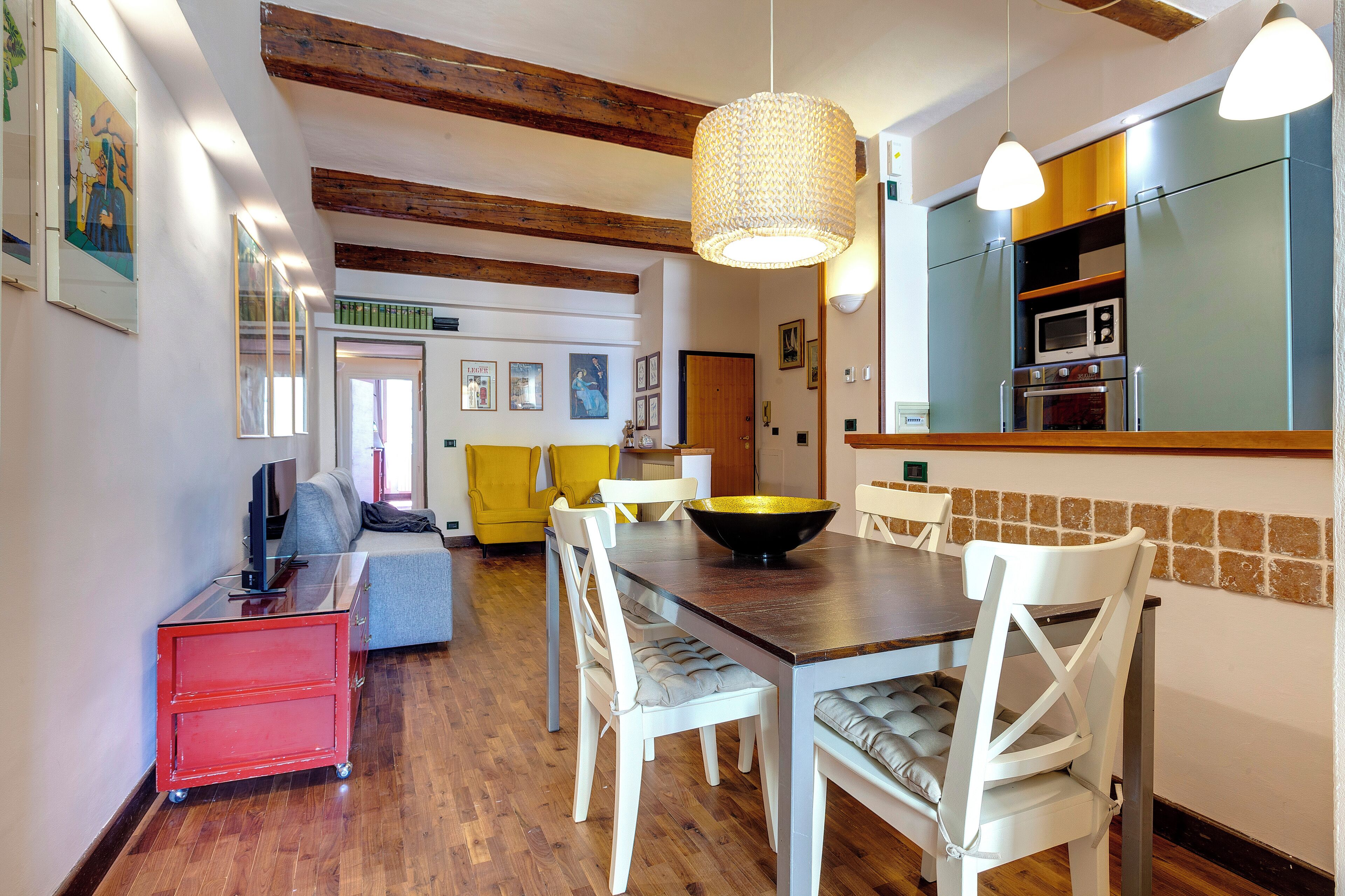 Un coin repas avec une table en bois, des chaises blanches, un buffet rouge et un canapé jaune.