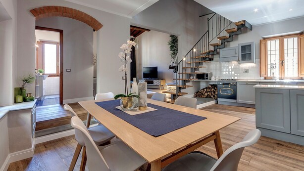 Una cucina moderna con mobili grigi, una scala in legno e un'area pranzo con tavolo e sedie.