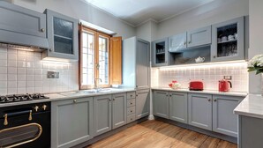 Una cucina con mobili grigi, un forno nero, una finestra e un piano di lavoro con un bollitore rosso.