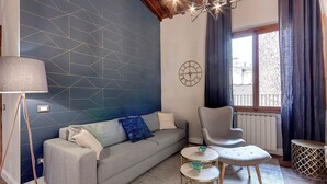 Un soggiorno moderno con parete a motivi geometrici, un divano con cuscini, un tavolino, una poltrona e una lampada.