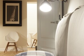 Une chambre à coucher avec un lit, une chaise blanche, un tableau encadré au mur et une porte avec un luminaire.