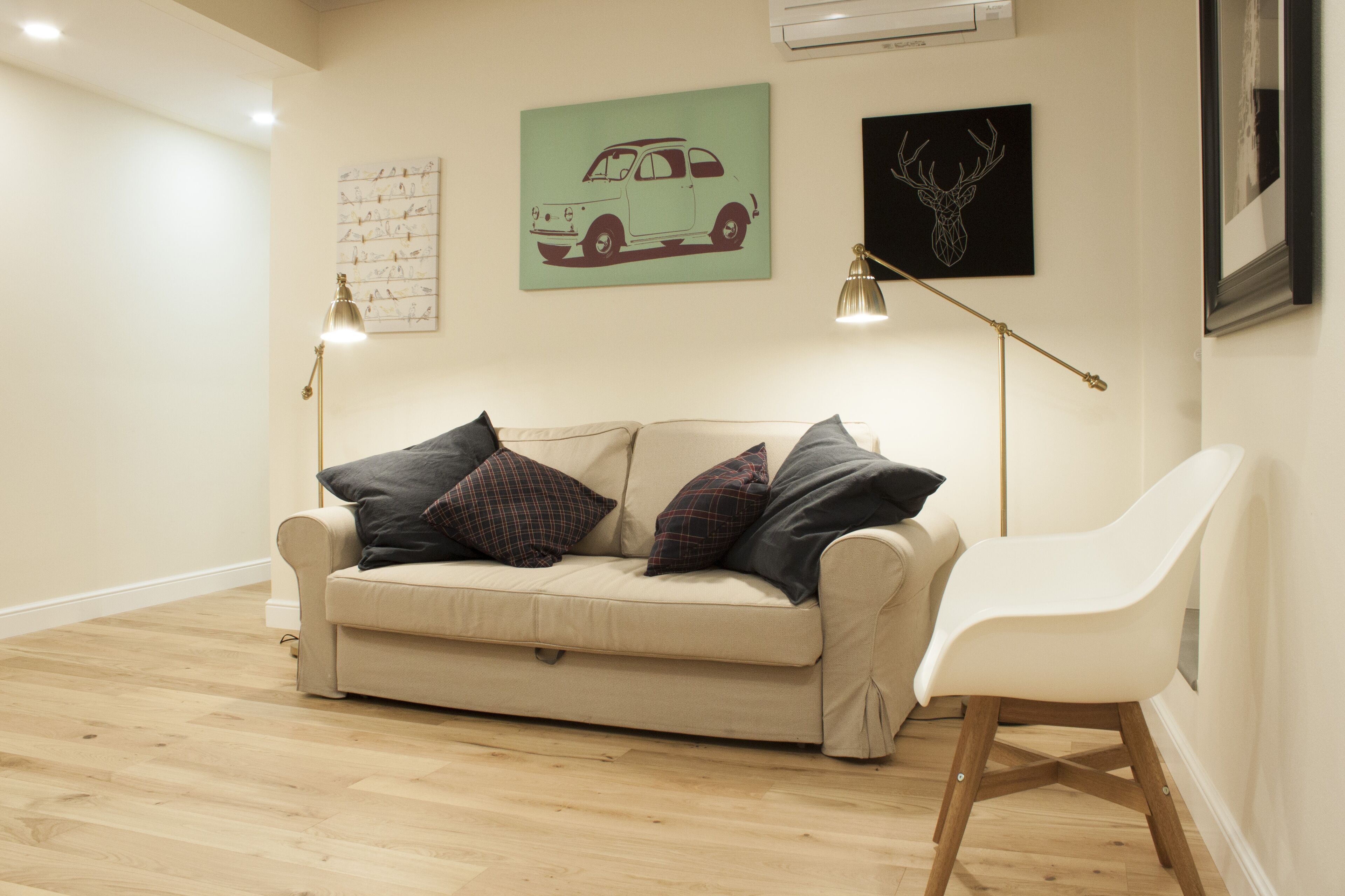 Ein Wohnzimmer mit einem beigen Sofa, zwei Stehlampen und einem weißen Sessel.