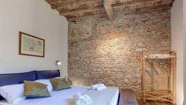 Ein Schlafzimmer mit Steinwand, Holzbalkendecke, einem Bett mit Kissen, einem hängenden Kleiderständer und einer gerahmten Karte an der Wand.