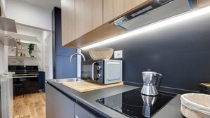 A modern kitchen with a black induction cooktop, a coffee maker, and a basket on the countertop. - Mamo Florence - Guido Monaco Apartment (Florence)