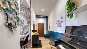 A hallway with a piano, a desk with a lamp, and wall art. - Mamo Florence - Guido Monaco Apartment (Florence)