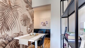 A dining area with a white table, black chairs, a bookshelf with books and a printer, and a wall with a tropical leaf wallpaper. - Mamo Florence - Guido Monaco Apartment (Florence)