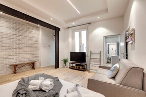 Un salon moderne avec un mur en briques, un plancher en bois, un canapé, une télévision et une petite plante.