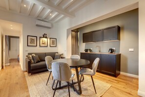 A modern living room with a round dining table, grey sofas, and a dark kitchen with built-in cabinets. - Mamo Florence - La Badessa Apartment (Florence)