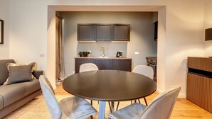 A modern living room with a round table and grey chairs, a grey sofa, and a kitchen area with cabinets and a sink. - Mamo Florence - La Badessa Apartment (Florence)