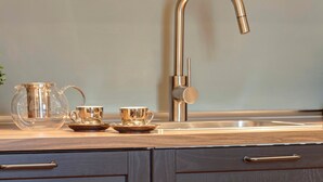 A kitchen with a stainless steel faucet, a glass pitcher, and two cups on a wooden countertop. - Mamo Florence - La Badessa Apartment (Florence)