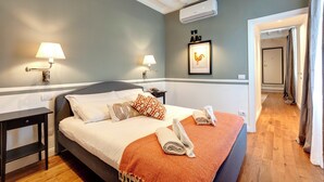 A neatly made bed with a white and orange blanket, two bedside lamps, and a framed rooster picture on the wall. - Mamo Florence - La Badessa Apartment (Florence)